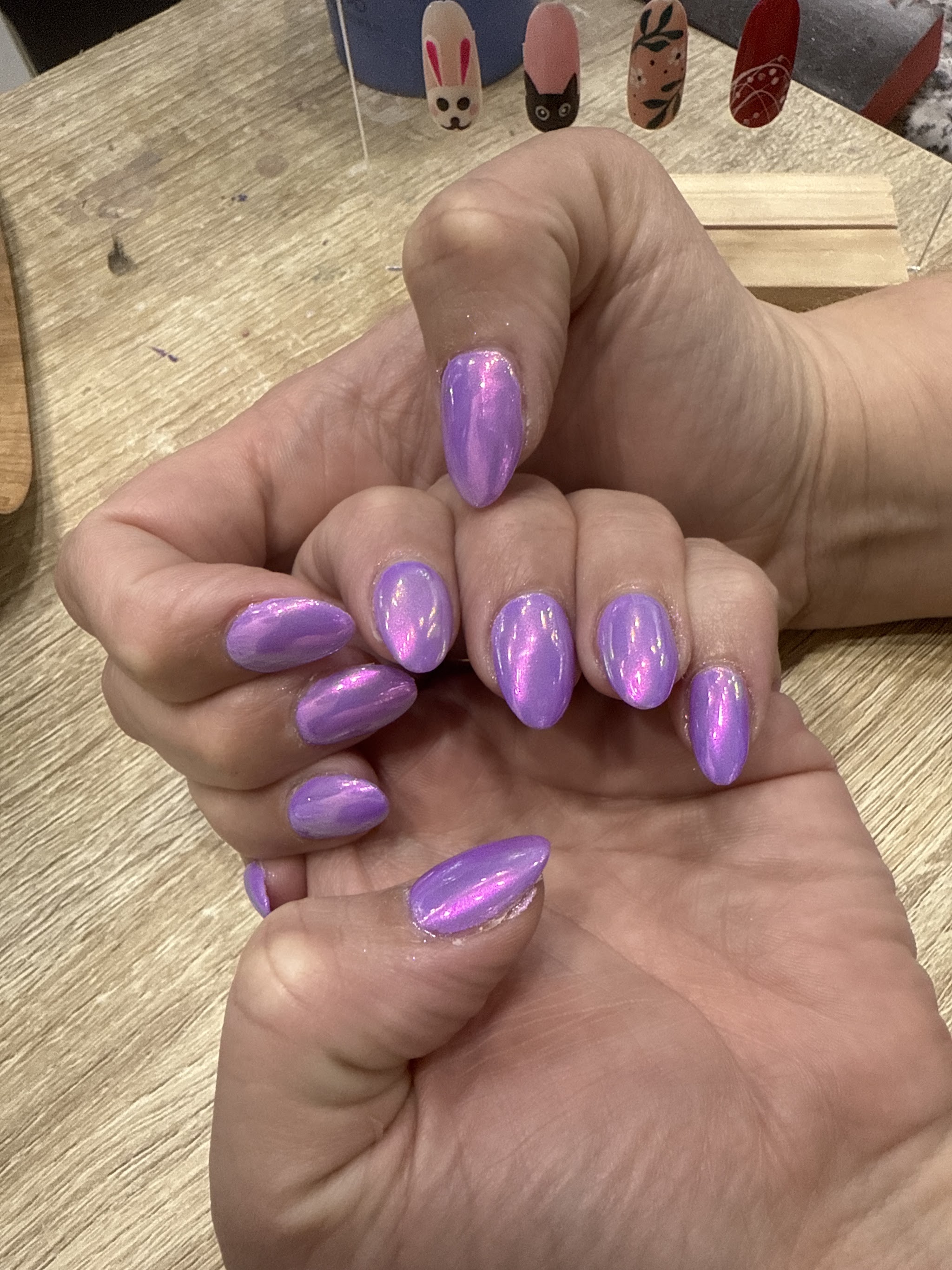 Lilac chrome almond nails, with sample nail art designs on the workbench behind