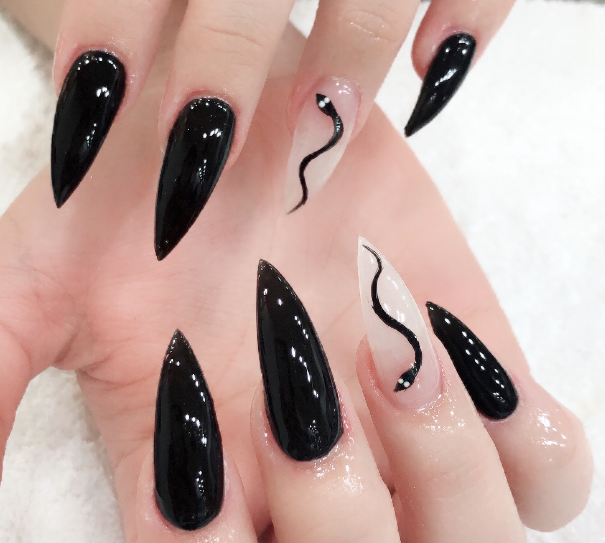 Glossy black stiletto nails with a hand-painted snake accent nail