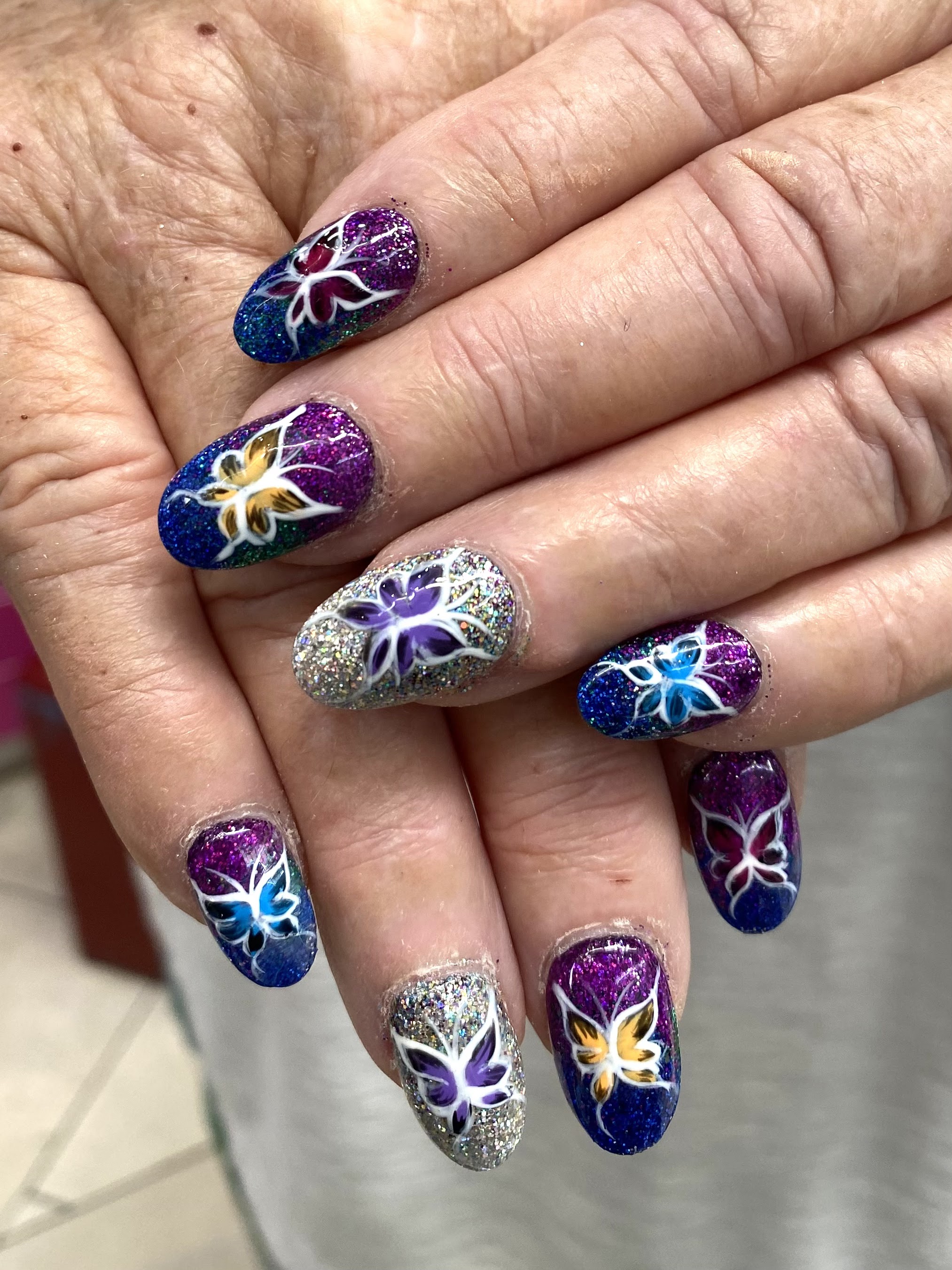 Purple and blue galaxy glitter nails with hand-painted butterflies and flowers